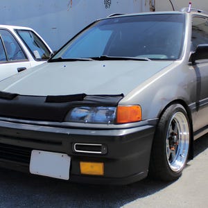 May include: A grey Honda Civic hatchback with a black bonnet scoop and aftermarket wheels. The car has a black bumper and a silver grille.