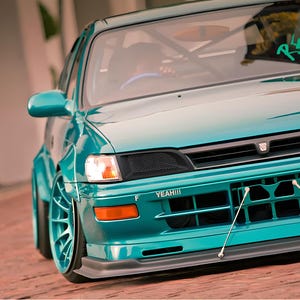 May include: A teal blue car with a black grille and a black bumper. The car has a black spoiler and a black rear diffuser. The car has a sticker on the windscreen that says "Real Love".