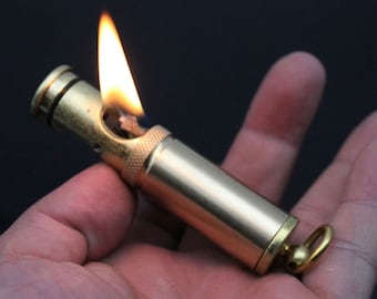 May include: A brass lighter with a flame coming out of the top. The lighter has a small ring on the end.