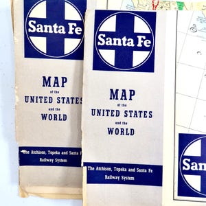 May include: Two vintage Santa Fe Railway maps of the United States and the World. The maps have a white background with blue text and a blue Santa Fe logo. The text includes "MAP of the UNITED STATES and the WORLD."