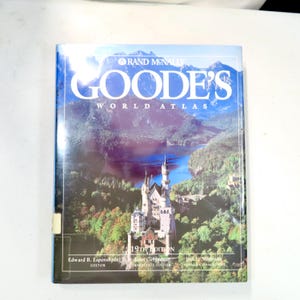 May include: A hardcover copy of Goode's World Atlas, 19th Edition. The cover features a scenic landscape with a castle and mountains. The title is in large white letters, with the Rand McNally logo at the top.
