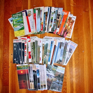 May include: A collection of vintage Missouri highway maps, some with the text "Missouri Highway Map" and "Missouri 1970". The maps are arranged in a stack, with the oldest maps on the bottom and the newest maps on the top.
