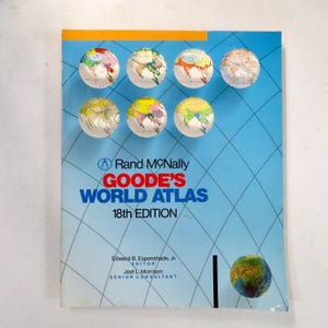 May include: A blue cover of Goode's World Atlas, 18th Edition, with a grid pattern and several small globe illustrations. The title is in large, bold letters. The cover also includes the names of the editor and senior consultant.