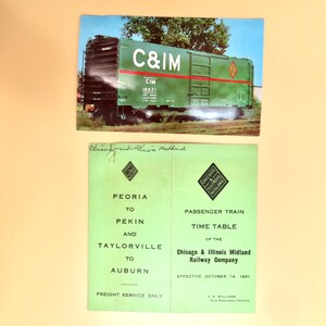 May include: Two vintage items: a postcard featuring a green C&IM freight train car with red accents and the text "C&IM CIM 16021", and a green passenger train timetable from the Chicago & Illinois Midland Railway Company.