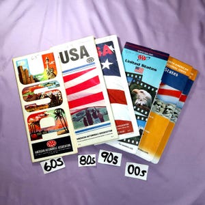 May include: Five vintage AAA road atlases for the United States, with covers featuring the American flag and iconic landmarks. The atlases are dated from the 1960s to the 2000s.