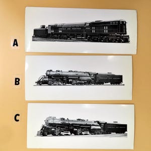 May include: Three black and white prints of Norfolk and Western trains. The prints are on white backgrounds and feature different train models. The trains are labeled with numbers and the words "Norfolk and Western".