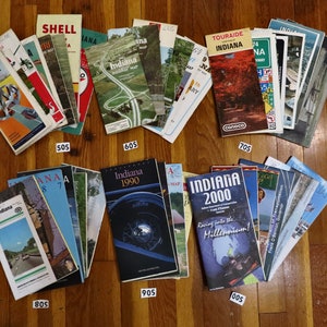 May include: A collection of vintage Indiana road maps, organized by decade, from the 1950s to the 2000s. The maps are in various sizes and colors, with some featuring illustrations of cars and landmarks.