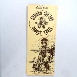 May include: A vintage brochure titled "Guide to the Lander Cut-Off Oregon Trail" from 1968. The brochure features illustrations of covered wagons, oxen, and text in a classic, sepia-toned design. The brochure is folded.
