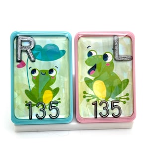 May include: Two light blue and pink tiles with a frog illustration and the letters R and L. The tiles also have the number 135 on them.