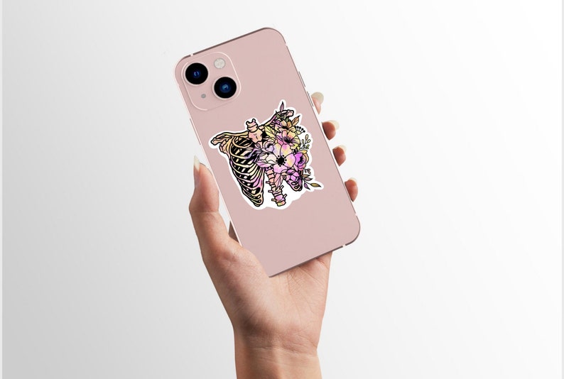 May include: A pink phone case featuring a sticker of a floral ribcage design. The sticker is in a watercolour style with pink, yellow and purple flowers.