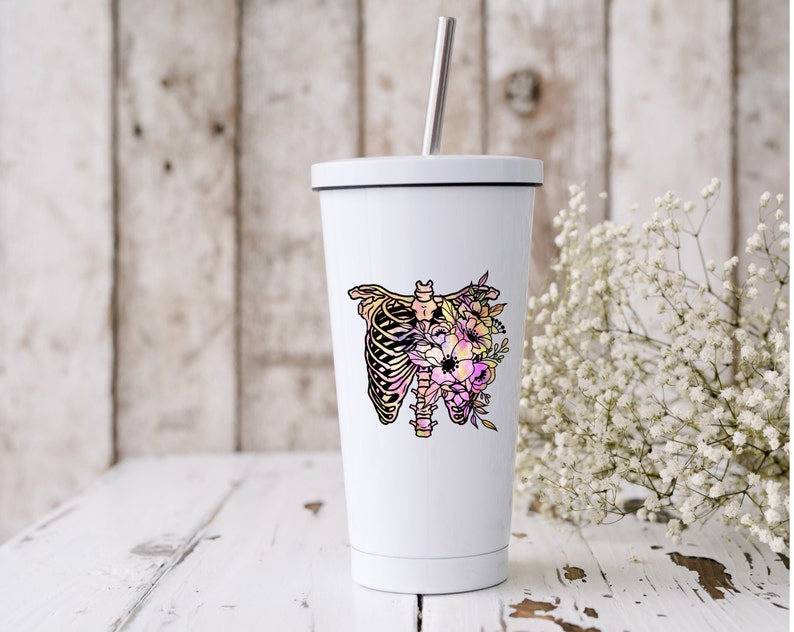 May include: White stainless steel tumbler with a floral design featuring a ribcage and flowers in shades of pink, yellow, and purple.