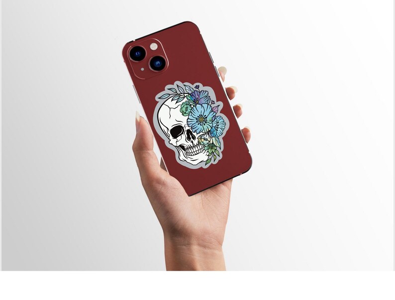 May include: A red phone case with a white skull sticker featuring blue and purple flowers. The skull is surrounded by leaves and vines.