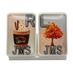 May include: Two white ceramic tiles with a fall theme. The left tile features a pumpkin spice latte with whipped cream and cinnamon sticks. The right tile features a cartoon tree with orange and yellow leaves. Both tiles have the letters "JMS" and "RL" in silver.