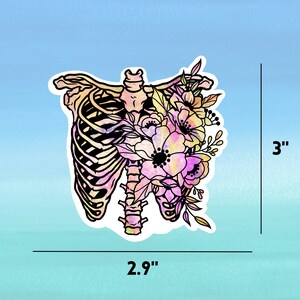 May include: A colourful sticker featuring a watercolour-style illustration of a ribcage with flowers growing from it. The ribcage is outlined in black and the flowers are in shades of pink, yellow, and orange. The sticker is 2.9 inches wide and 3 inches tall.