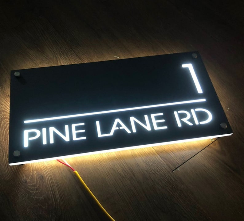 Pu&ograve; includere: Un cartello rettangolare nero con lettere LED bianche che recita "1 PINE LANE RD".