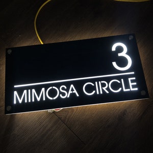 Pu&ograve; includere: Un cartello rettangolare nero con lettere bianche. Il cartello recita "3 Mimosa Circle".