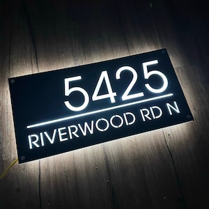 Pu&ograve; includere: Cartello nero per numeri civici con lettere bianche illuminate. Il cartello indica "5425 RIVERWOOD RD N".
