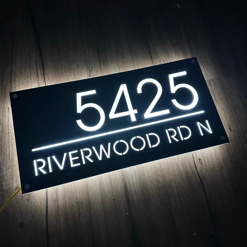 Pu&ograve; includere: Cartello nero per numeri civici con lettere bianche illuminate. Il cartello indica "5425 RIVERWOOD RD N".