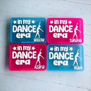 May include: Four rectangular plastic boxes in blue and pink. Each box has the text "in my DANCE era" with a star and a dancer silhouette in white. Names Willow, Sanaya, Azaria, and Ruby are printed below.