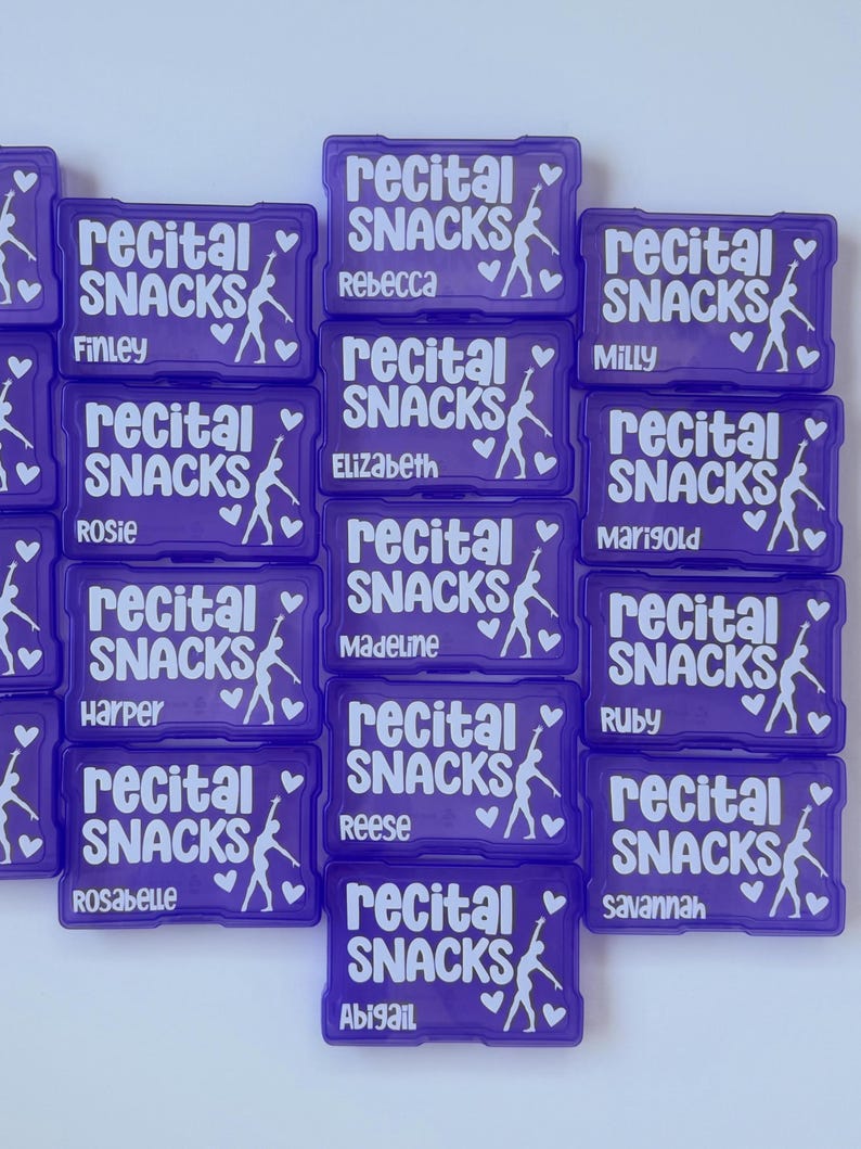 Pode incluir: Uma cole&ccedil;&atilde;o de recipientes retangulares de pl&aacute;stico roxo para lanches, cada um com o texto branco "recital SNACKS", a silhueta de um dan&ccedil;arino e dois cora&ccedil;&otilde;es. Cada recipiente &eacute; personalizado com um nome diferente, incluindo Rebecca, Finley, Milly, Rosie, Marigold, Harper, Madeline, Ruby, Rosabelle, Reese, Savannah e Abigail.