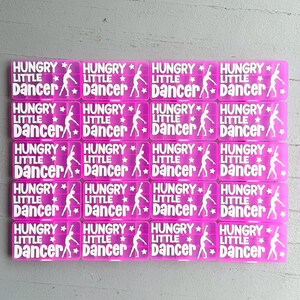 May include: A grid of pink rectangular stickers, each bearing the white text "HUNGRY LITTLE DANCER". The design includes a dancer silhouette and stars. The stickers are suitable for various craft projects.