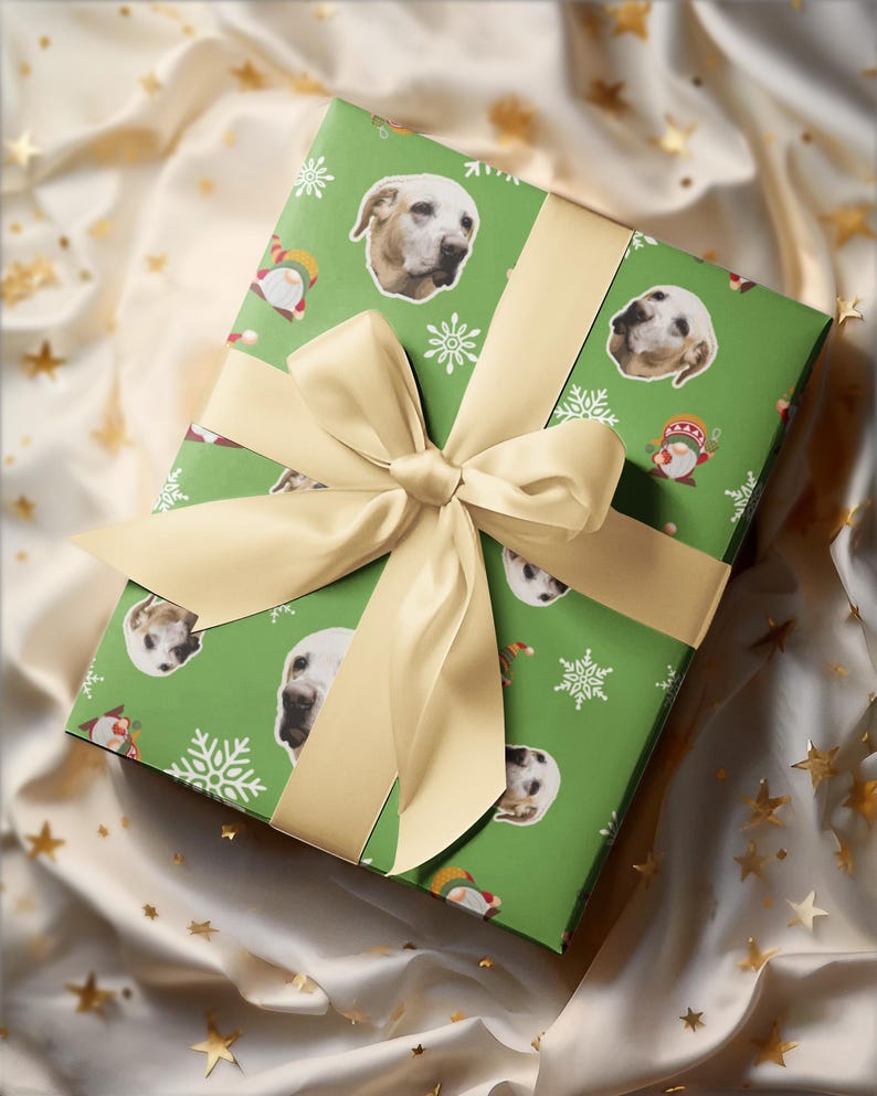 May include: A wrapped gift with green wrapping paper featuring dog faces, snowflakes, and gnome illustrations. The gift is tied with a cream-colored ribbon and bow. The background is a cream-colored fabric with gold star accents.