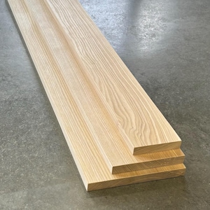 Op de afbeelding: Vier stukken onbewerkt, lichtbruin hout planken gestapeld op elkaar. De planken hebben een natuurlijke houtnerf patroon.