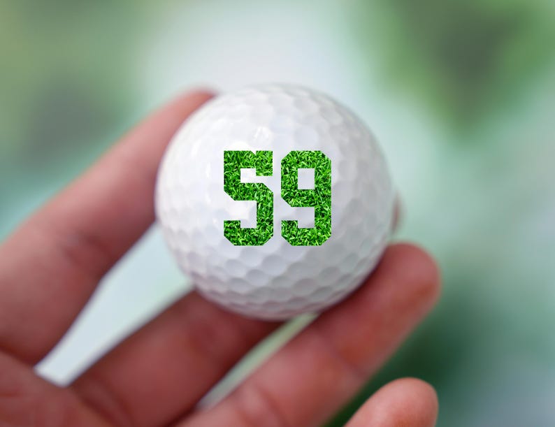 May include: A white golf ball with the number 59 printed on it in green grass.