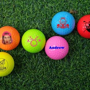 May include: Six personalized golf balls with different designs. The balls are yellow, orange, pink, green, red, and blue. The designs include a deer, a golfer, a crown, a name, and a golf club.