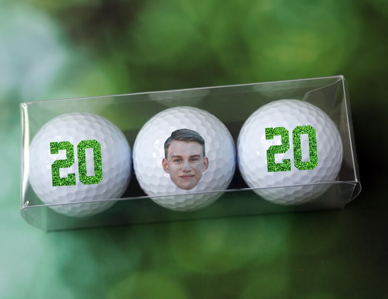 May include: Three white golf balls with green glitter numbers '20' on two of the balls. The third ball has a photo of a person's face on it.