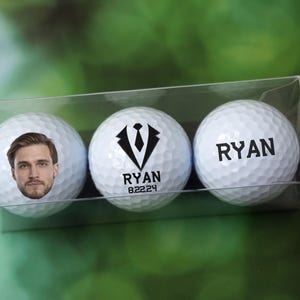 May include: Three white golf balls in a clear plastic box. One ball has a black and white image of a tuxedo with a tie and the name "RYAN 82224" printed on it. Another ball has the name "RYAN" printed on it. The third ball has a photo of a man's face printed on it.