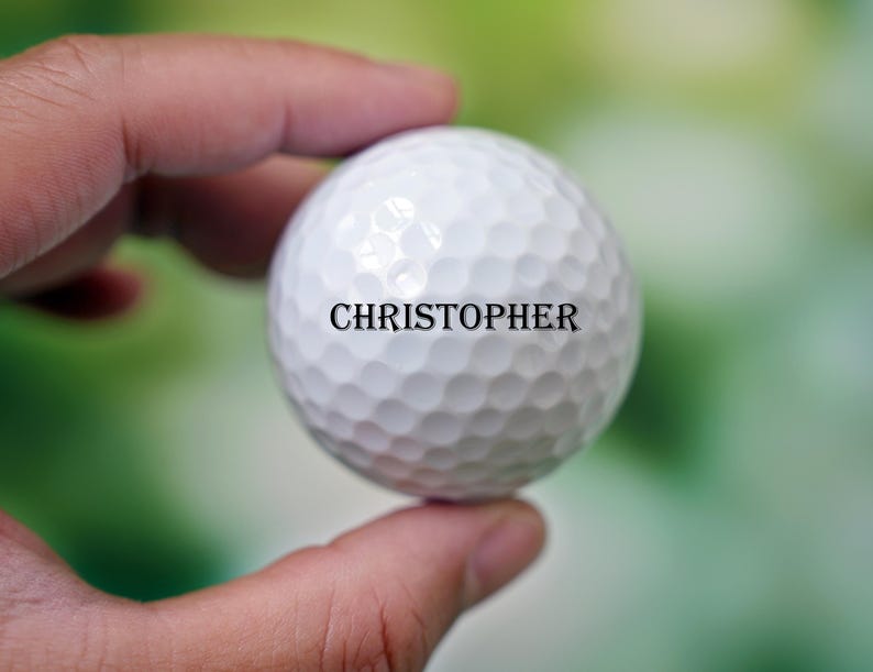 Może przedstawiać: Biała piłka golfowa z nadrukowanym imieniem "CHRISTOPHER".