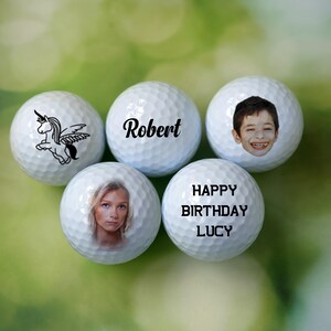 Może przedstawiać: Pięć białych piłek golfowych z personalizowanymi wzorami. Jedna piłka ma jednorożca ze skrzydłami, druga ma napis "Robert", trzecia ma twarz dziecka, czwarta ma napis "Happy Birthday Lucy", a ostatnia ma twarz kobiety.