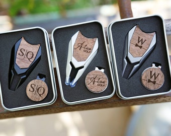 May include: Three silver golf ball marker sets in black, silver, and wood boxes. Each set includes a golf ball marker, a divot tool, and a magnetic ball marker holder. The ball markers are engraved with the initials "S/Q", "Alan Golf", and "W" with a bowtie.