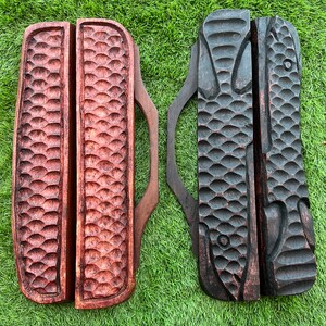 May include: Two wooden knife holders with a fish design. The holder on the left is a light brown color and the holder on the right is a dark brown color. Both holders have a handle and are labeled "MEDIUM".