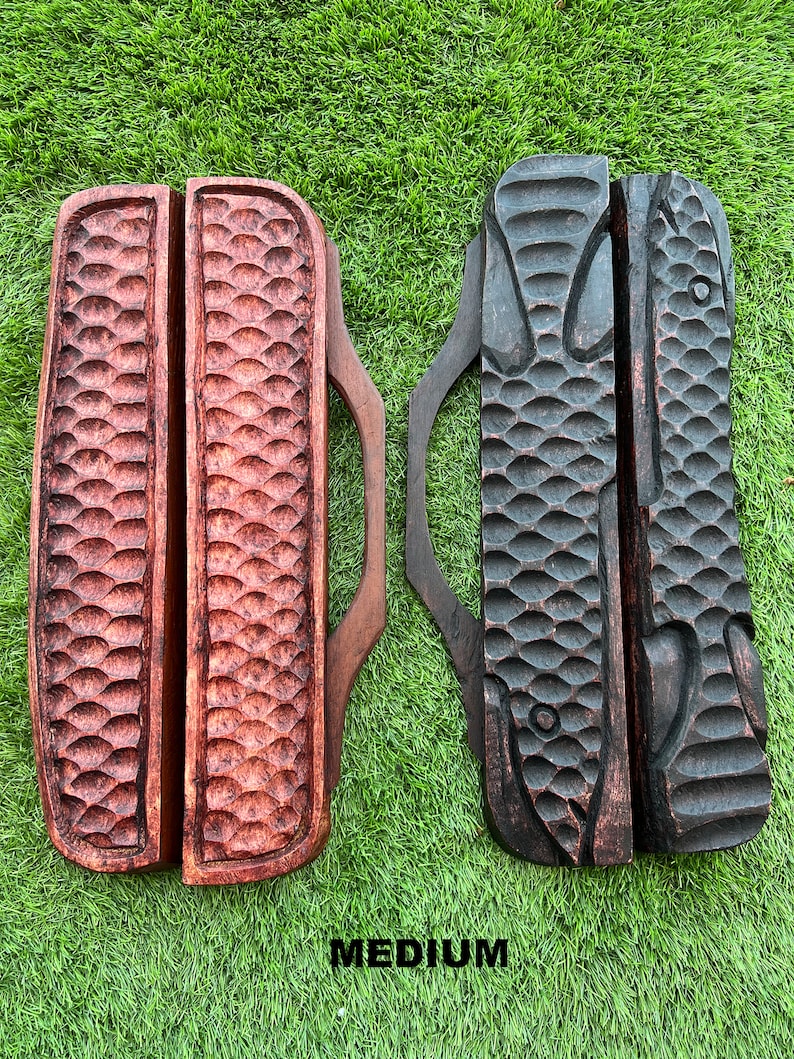 May include: Two wooden knife holders with a fish design. The holder on the left is a light brown color and the holder on the right is a dark brown color. Both holders have a handle and are labeled "MEDIUM".