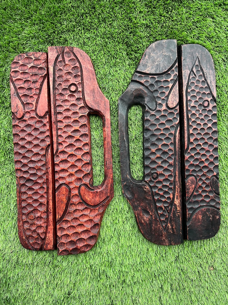 May include: Two wooden wall hangings with a carved fish design. One is dark brown and the other is a reddish brown.