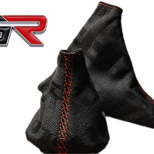 May include: Two black gear shift knobs with orange stitching. The knobs have a textured fabric surface and are designed to fit a standard shift lever.