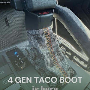 May include: Close-up of a car's gear shift with a custom boot cover. The boot cover has a snakeskin pattern with orange stitching. The text "4 GEN TACO BOOT is here" is visible at the bottom of the image.