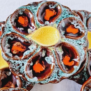 Peut inclure: Assiettes à huîtres en céramique avec six compartiments individuels et une section centrale en forme de citron. Les assiettes présentent un glaçage marron, orange et turquoise, créant une esthétique vintage. Idéales pour servir des huîtres.