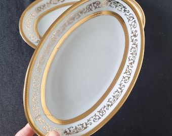 May include: Two oval white porcelain dishes featuring a wide gold rim and an intricate gold filigree scrollwork pattern along the border. The dishes have a smooth, glossy finish and a clean, simple center design with no additional markings.