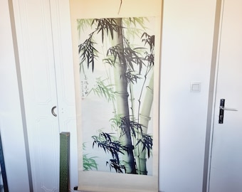 May include: A bamboo scroll painting with green and black bamboo stalks and leaves. The artwork features a traditional Asian style with calligraphy. The scroll is hanging on a wall with a wooden bar at the bottom.
