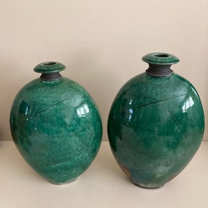 May include: Two green ceramic vases with a crackled glaze finish. The vases are oval shaped and have a wide opening at the top.