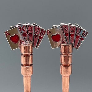 May include: Two copper bottle stoppers with a design of playing cards in a fan shape. The cards are silver with red hearts and the letters A, K, Q, J, 10 are visible.