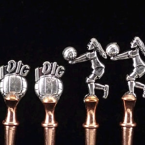 May include: Four metal stirring spoons with copper-toned stems. Two spoons feature a silver-toned volleyball with the text I DIG on top. The other two spoons feature a silver-toned figure of a volleyball player in a digging motion.