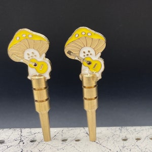 May include: Two gold-colored metal pipes with mushroom-shaped tops. The mushrooms are painted yellow with white accents and feature a small guitar design.