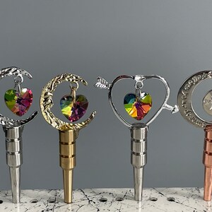 May include: Five different bottle stoppers with a moon, heart, and star design. Each stopper features a dangling crystal heart charm.