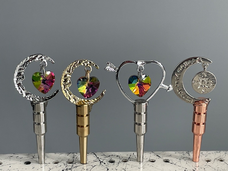 May include: Five different bottle stoppers with a moon, heart, and star design. Each stopper features a dangling crystal heart charm.