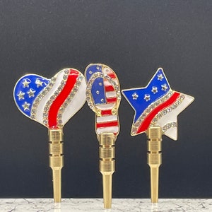 May include: Three gold-colored metal pins with red, white, and blue enamel designs. The designs are a heart, a flip-flop, and a star. Each design is decorated with rhinestones.