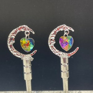 May include: Two silver crescent moon charms with iridescent heart-shaped crystals hanging from them. The charms are attached to silver posts.